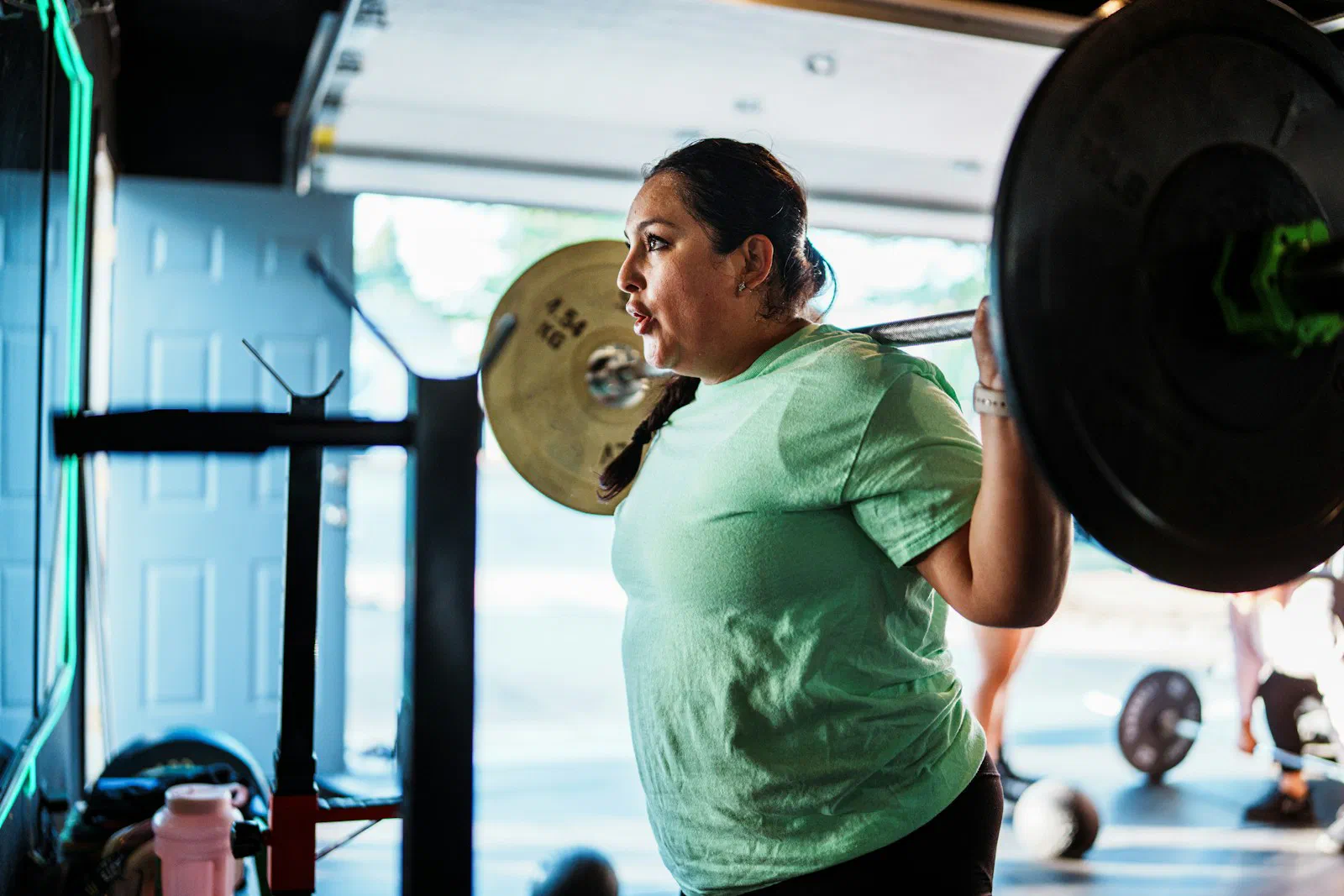 A woman performing a back squat with a loaded barbell in natural light, focused mid-lift